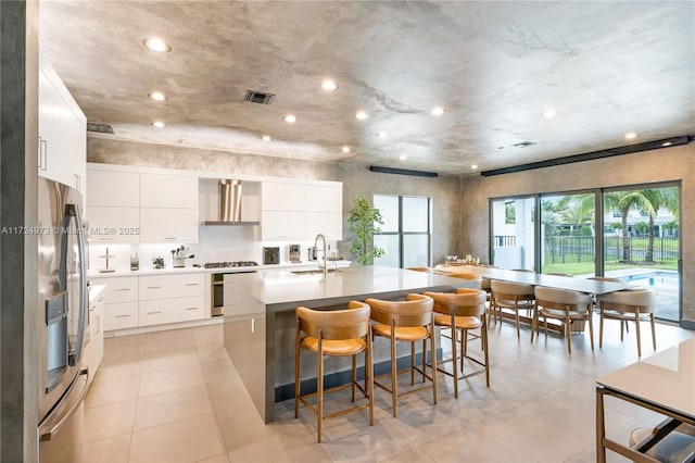 kitchen featuring wall chimney range hood, sink, a breakfast bar, white cabinets, and a center island with sink