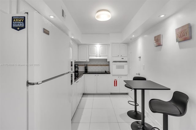 kitchen featuring white cabinetry, white appliances, light tile patterned floors, and decorative backsplash