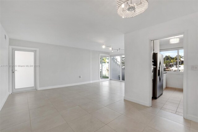 empty room featuring a water view, light tile patterned floors, plenty of natural light, and an inviting chandelier