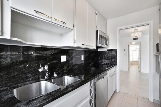 kitchen with light tile patterned floors, white cabinets, decorative backsplash, stainless steel appliances, and a sink