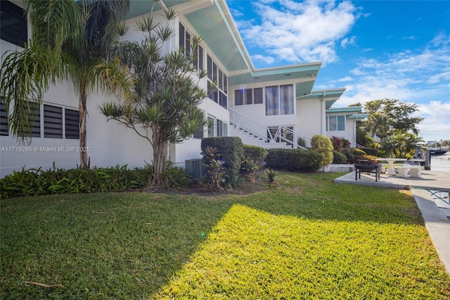 view of property exterior featuring a sunroom, stucco siding, a lawn, and stairs