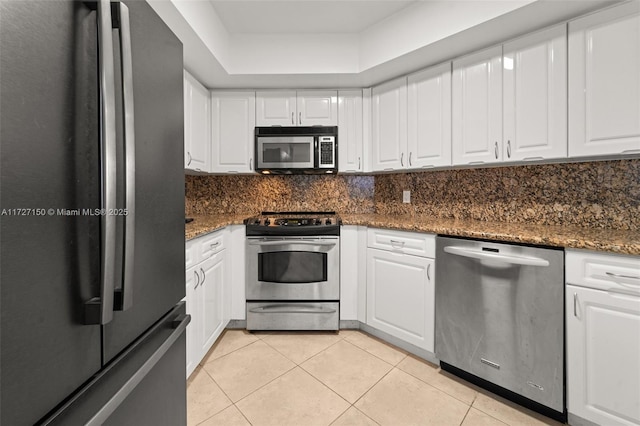 kitchen with light tile patterned floors, dark stone countertops, stainless steel appliances, and white cabinetry