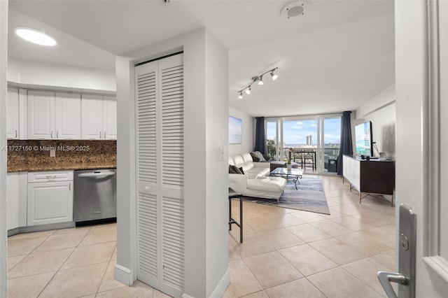 interior space featuring light tile patterned floors, white cabinetry, backsplash, dark stone counters, and stainless steel dishwasher