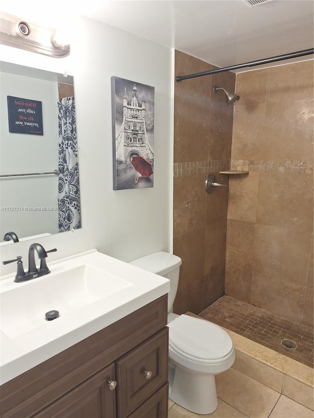 bathroom with tiled shower, tile patterned flooring, vanity, and toilet