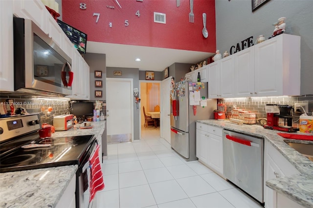 kitchen with white cabinets, appliances with stainless steel finishes, decorative backsplash, light stone counters, and light tile patterned floors