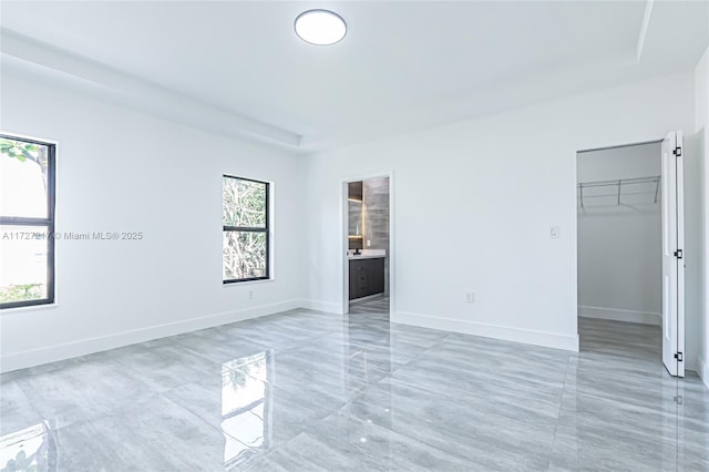 unfurnished bedroom featuring a walk in closet, baseboards, a closet, marble finish floor, and ensuite bath