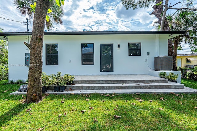 rear view of house featuring stucco siding, a lawn, and cooling unit