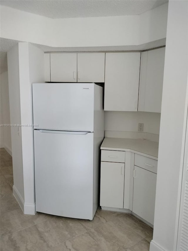 kitchen featuring a textured ceiling, white fridge, and white cabinetry