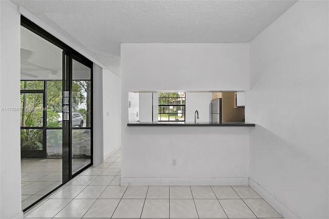 tiled spare room featuring a textured ceiling, a healthy amount of sunlight, floor to ceiling windows, and sink