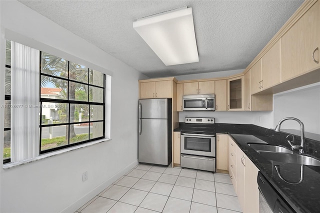 kitchen featuring sink, stainless steel appliances, light tile patterned floors, light brown cabinetry, and dark stone counters