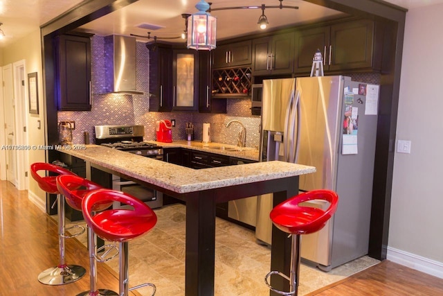 kitchen featuring kitchen peninsula, stainless steel appliances, decorative backsplash, wall chimney exhaust hood, and sink