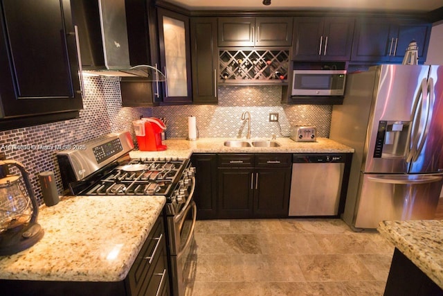 kitchen featuring light stone countertops, wall chimney exhaust hood, stainless steel appliances, decorative backsplash, and sink