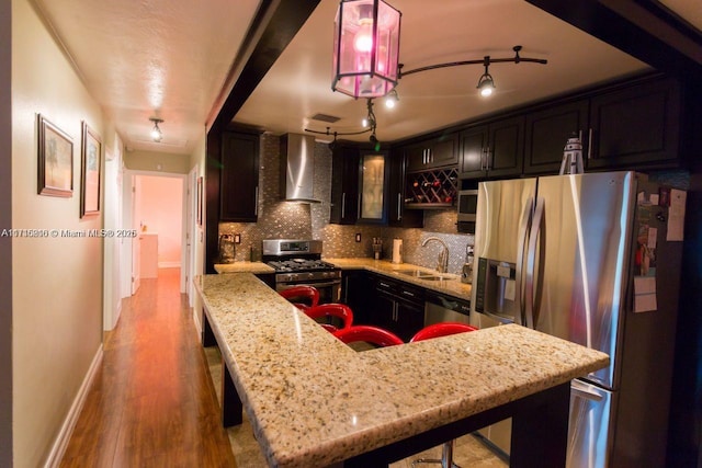 kitchen with tasteful backsplash, sink, appliances with stainless steel finishes, a breakfast bar area, and wall chimney exhaust hood