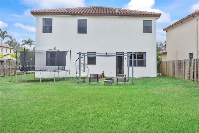 back of house with a fire pit, a lawn, and a trampoline