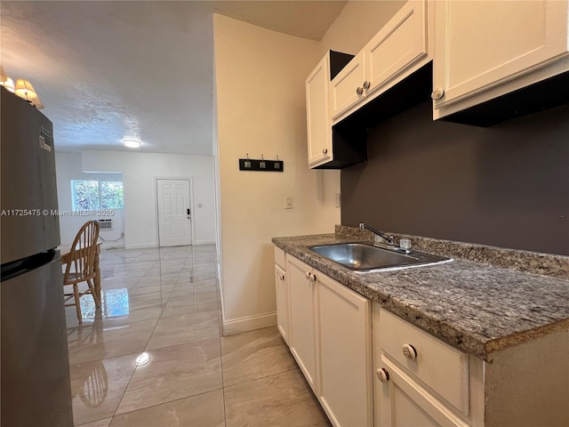 kitchen with stainless steel fridge, sink, dark stone countertops, and white cabinetry