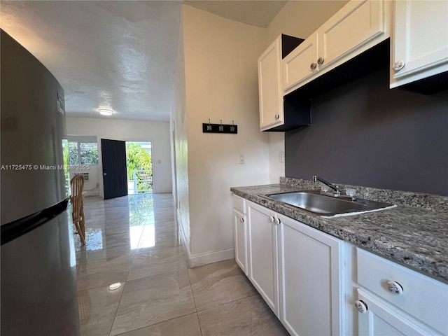 kitchen with baseboards, white cabinets, a sink, and freestanding refrigerator