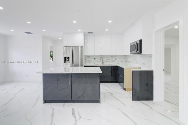 kitchen featuring appliances with stainless steel finishes, light stone countertops, a kitchen island, white cabinets, and sink