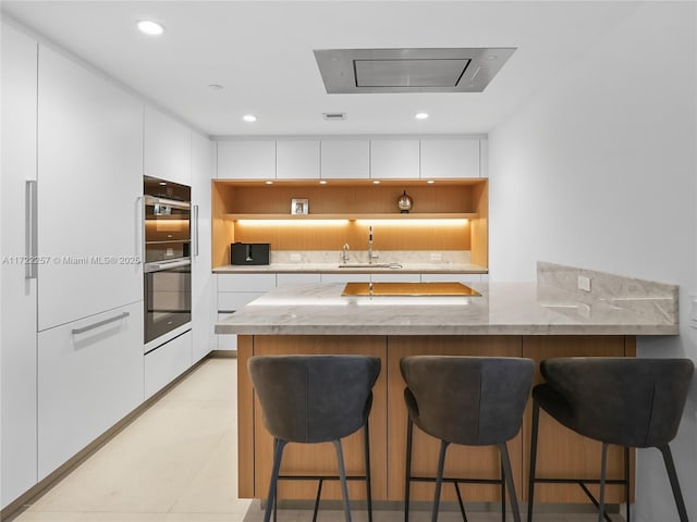 kitchen featuring white cabinets, kitchen peninsula, and double wall oven