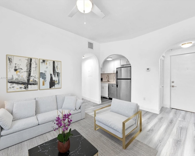 living area with light wood finished floors, visible vents, arched walkways, baseboards, and ceiling fan