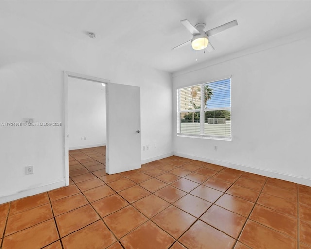 tiled empty room with ceiling fan and baseboards