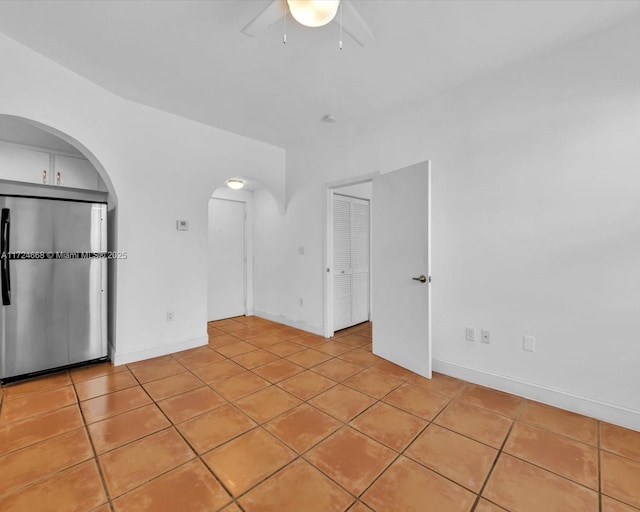 empty room with arched walkways, baseboards, ceiling fan, and light tile patterned floors