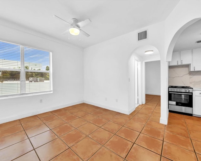 interior space with stainless steel range with gas cooktop, ceiling fan, tasteful backsplash, light tile patterned flooring, and white cabinets