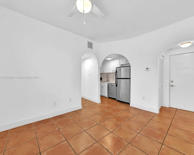 empty room with light tile patterned flooring, arched walkways, and ceiling fan