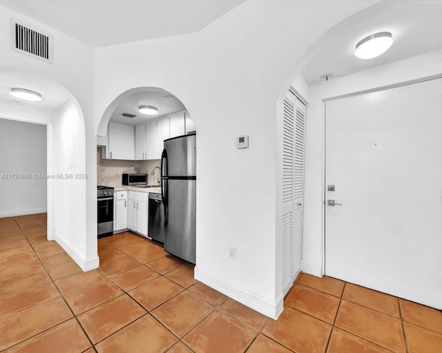 kitchen with white cabinets, decorative backsplash, light tile patterned flooring, and stainless steel appliances