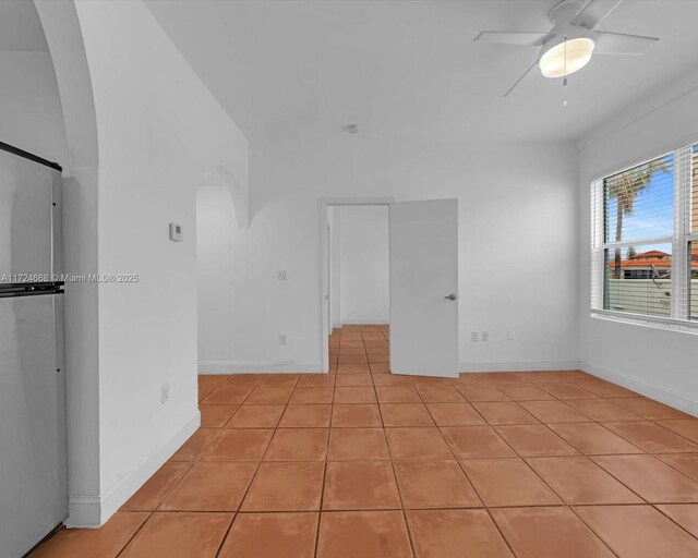 empty room featuring ceiling fan, baseboards, arched walkways, and light tile patterned floors