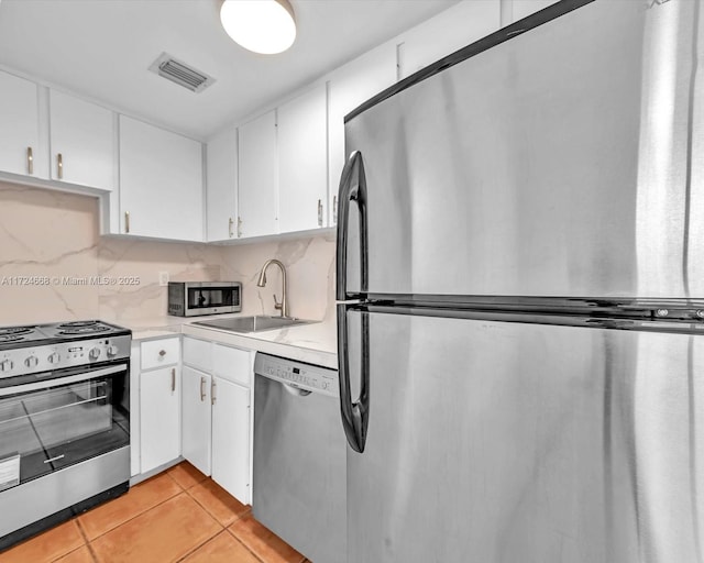 kitchen with stainless steel appliances, decorative backsplash, light tile patterned flooring, white cabinets, and sink