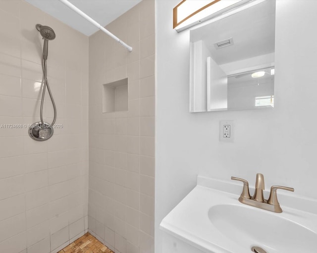 bathroom featuring a tile shower, vanity, and visible vents
