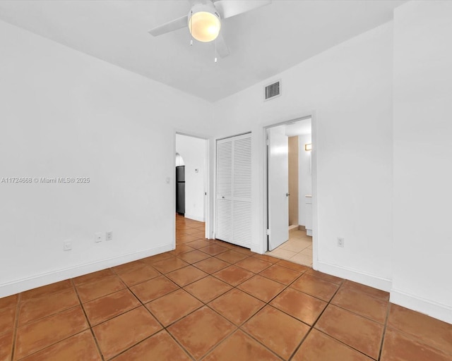 unfurnished bedroom featuring black refrigerator, connected bathroom, a closet, ceiling fan, and light tile patterned floors