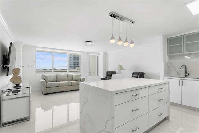 kitchen featuring decorative light fixtures, sink, crown molding, and white cabinetry