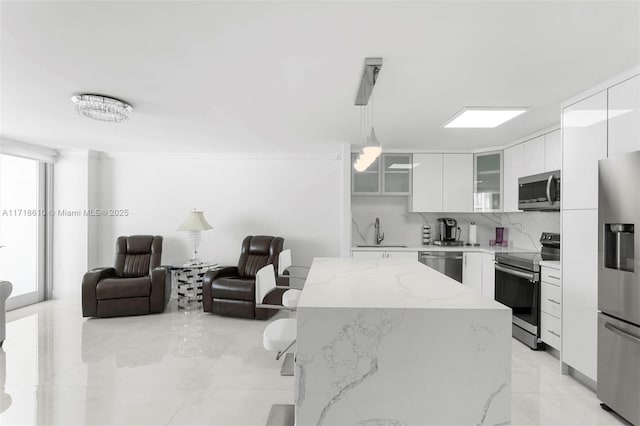 kitchen with white cabinetry, stainless steel appliances, hanging light fixtures, light stone counters, and sink