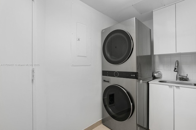 washroom featuring stacked washing maching and dryer, sink, electric panel, and cabinets