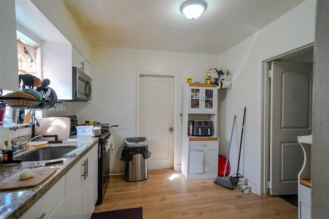 kitchen featuring white cabinetry, light wood-type flooring, stone countertops, black range with electric stovetop, and sink