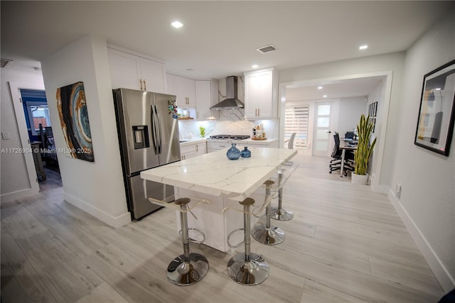 kitchen with white cabinetry, appliances with stainless steel finishes, wall chimney range hood, light stone counters, and a center island