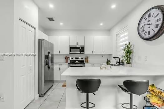 kitchen featuring white cabinetry, stainless steel appliances, kitchen peninsula, and a breakfast bar area