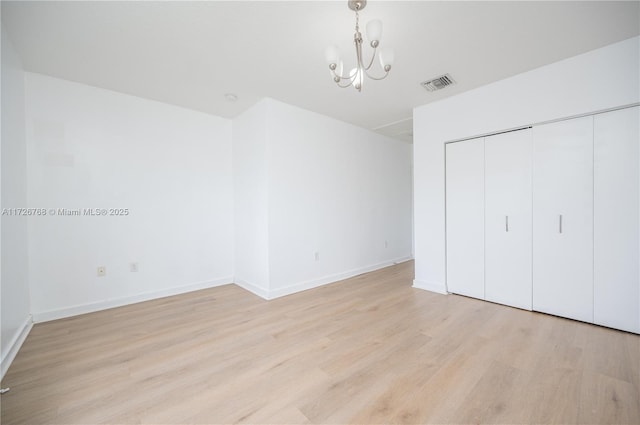 unfurnished bedroom featuring light wood-type flooring, a closet, and a notable chandelier