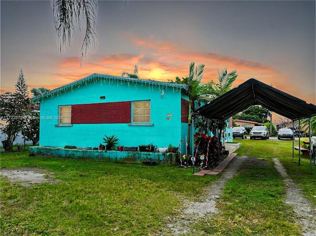 property exterior at dusk featuring a lawn and a carport