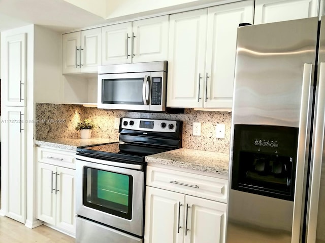 kitchen featuring stainless steel appliances, decorative backsplash, white cabinetry, and light stone countertops