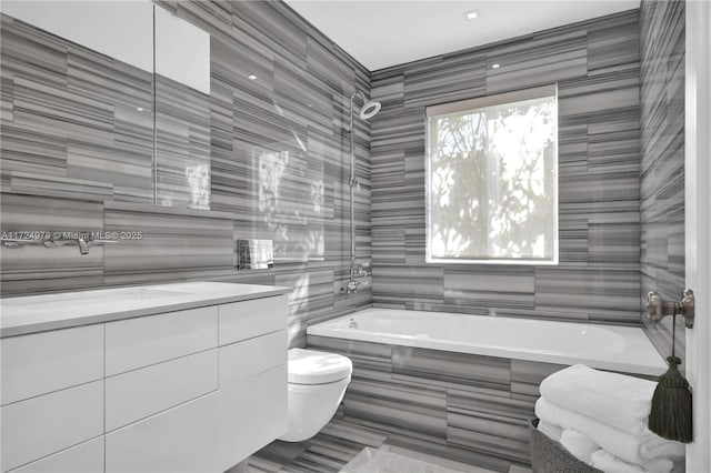 bathroom with toilet, tile walls, tiled bath, and vanity