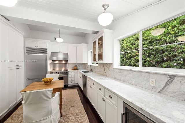 kitchen with light stone countertops, pendant lighting, white cabinets, high end appliances, and backsplash