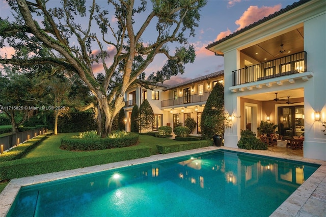 pool at dusk with a lawn, ceiling fan, and a patio area