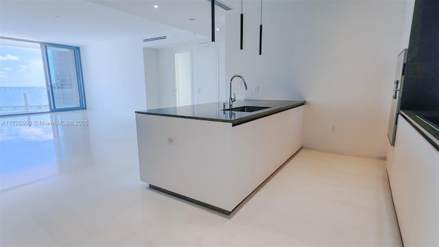 kitchen with a peninsula, a sink, white cabinetry, dark countertops, and modern cabinets