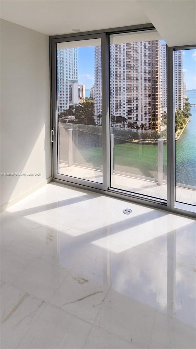 unfurnished room featuring a view of city, floor to ceiling windows, a water view, and baseboards