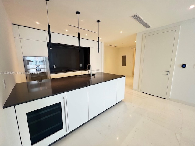 kitchen featuring white cabinets, decorative light fixtures, sink, electric panel, and a center island with sink