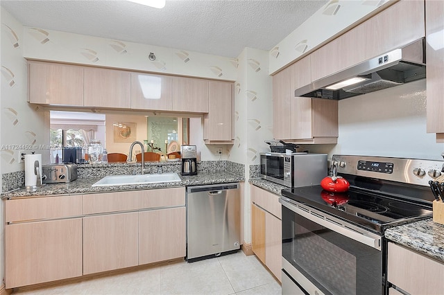 kitchen featuring stainless steel appliances, wall chimney exhaust hood, light brown cabinets, and sink