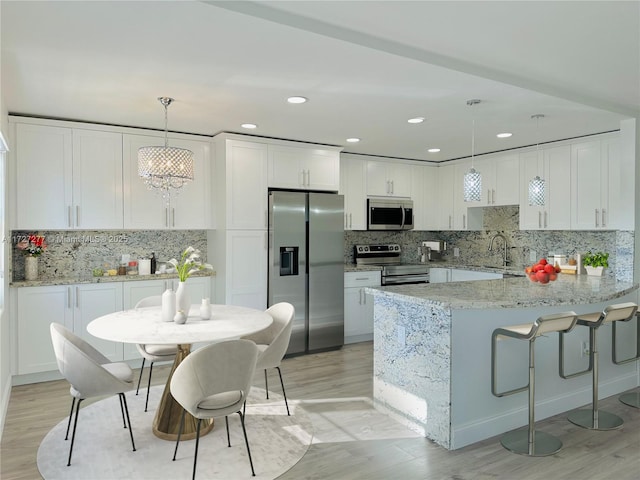 kitchen with white cabinetry, kitchen peninsula, stainless steel appliances, light stone countertops, and pendant lighting