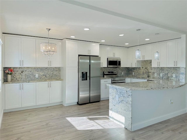 kitchen with white cabinets, stainless steel appliances, hanging light fixtures, kitchen peninsula, and light stone counters